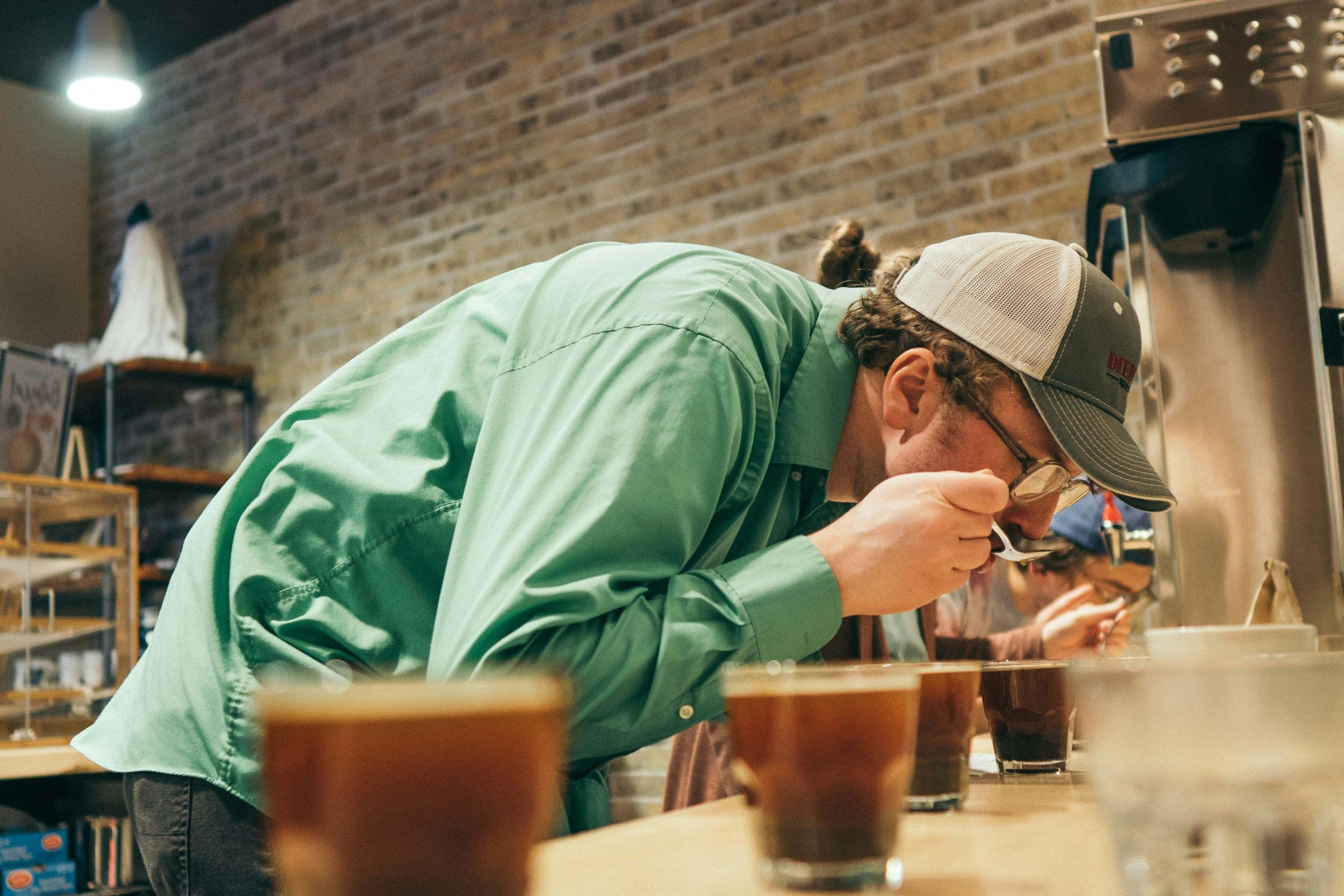 Person in a green shirt and cap working at a coffee bar with glasses of coffee.